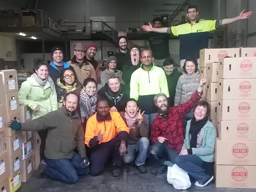 Group of volunteers posing in a warehouse with stacked cardboard boxes labeled Fair Food.